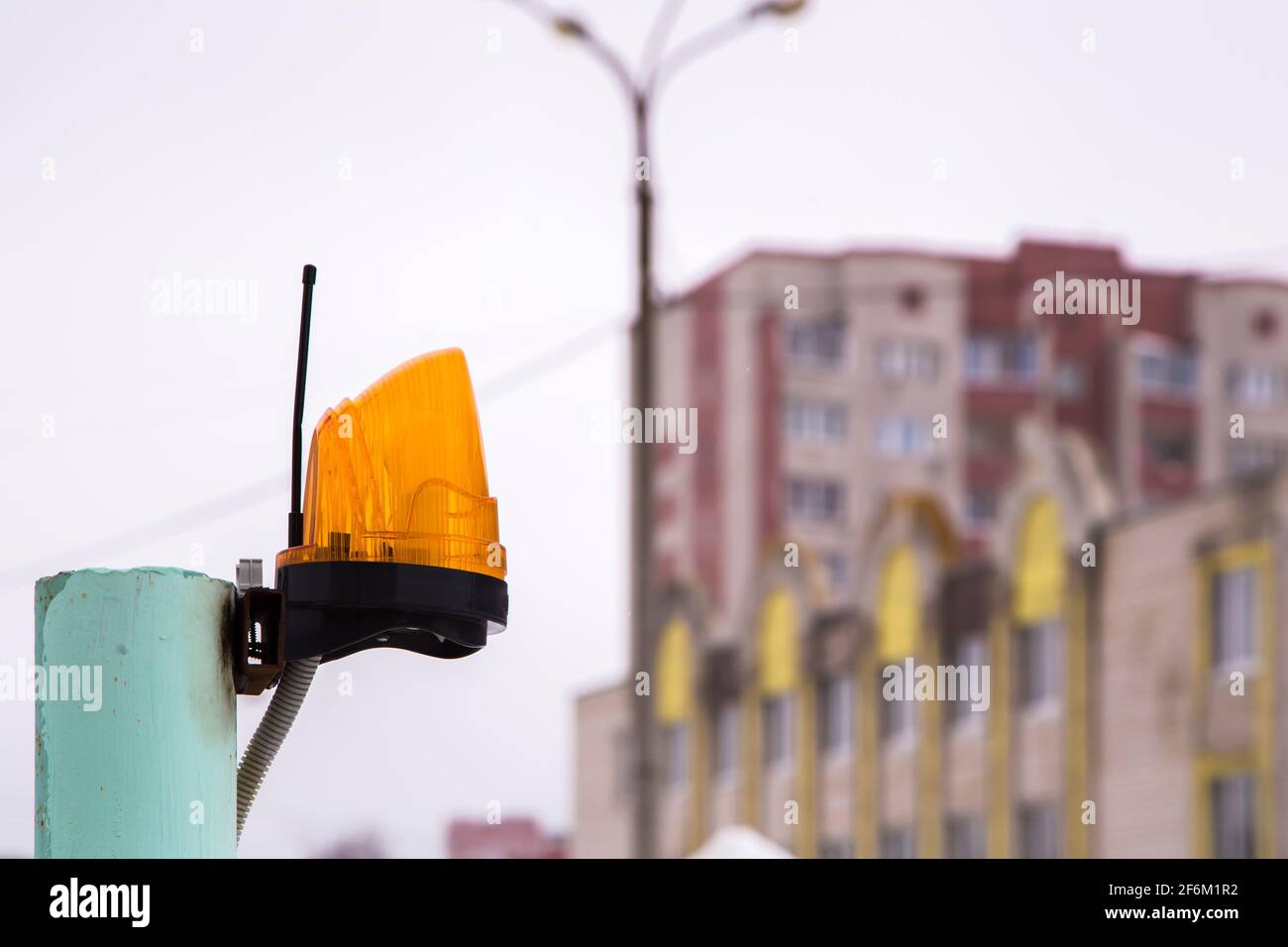 Lampe de signalisation jaune avec antenne sur tube métallique. En arrière-plan, hors foyer, un lampadaire et des bâtiments résidentiels. Ciel gris sombre. Banque D'Images