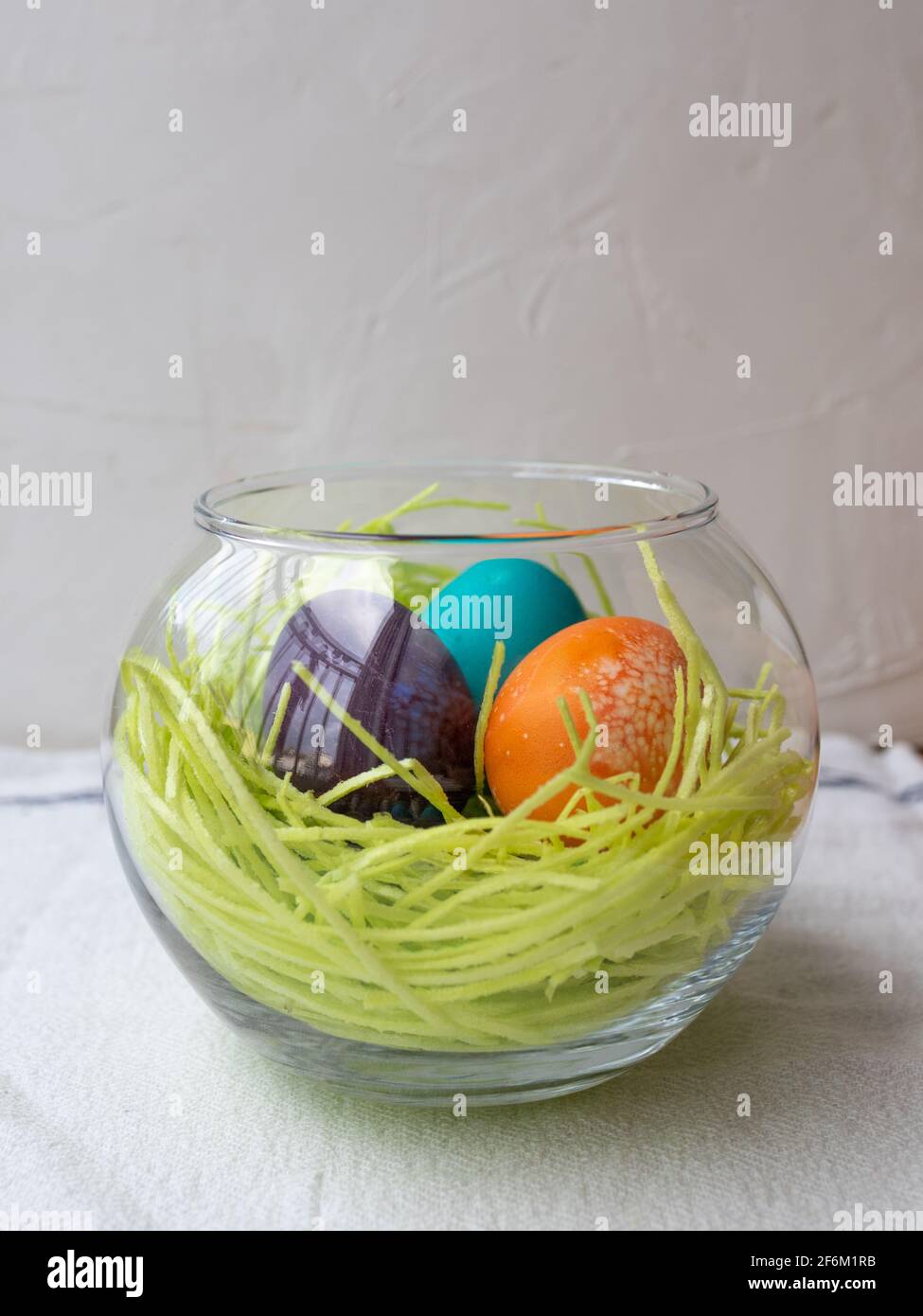 Bol en verre avec herbe comestible et trois œufs de pâques colorés (bleu, violet et orange) Banque D'Images