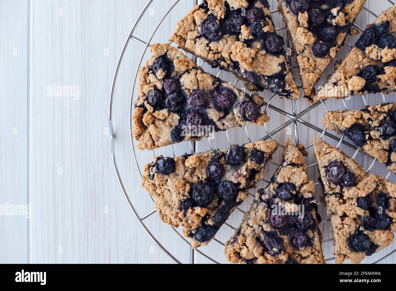 Scones aux myrtilles d'avoine fraîchement cuites sur un support de refroidissement sur fond de bois blanc, vue de dessus, plat. Pâte à base de légumes et de plantes, gros plan. Mets sucrés. Banque D'Images