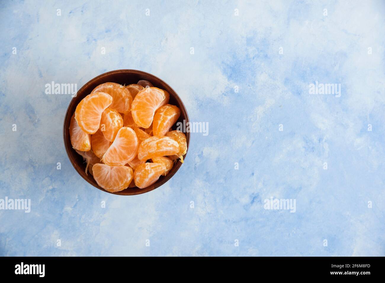 Tranches de mandarine dans un bol en bois sur fond bleu Banque D'Images