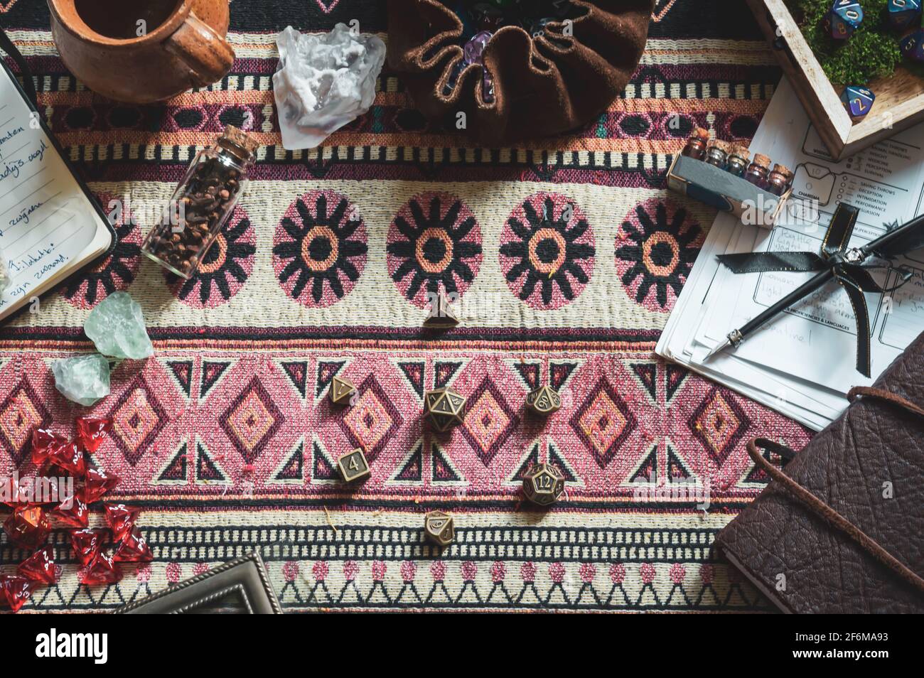 Vue du dessus de l'équipement de jeu de rôle, comme un sac de dés, des morceaux de papier, des cahiers, des cristaux, et un Quill noir, sur un plaid coloré. Modifié dans Banque D'Images
