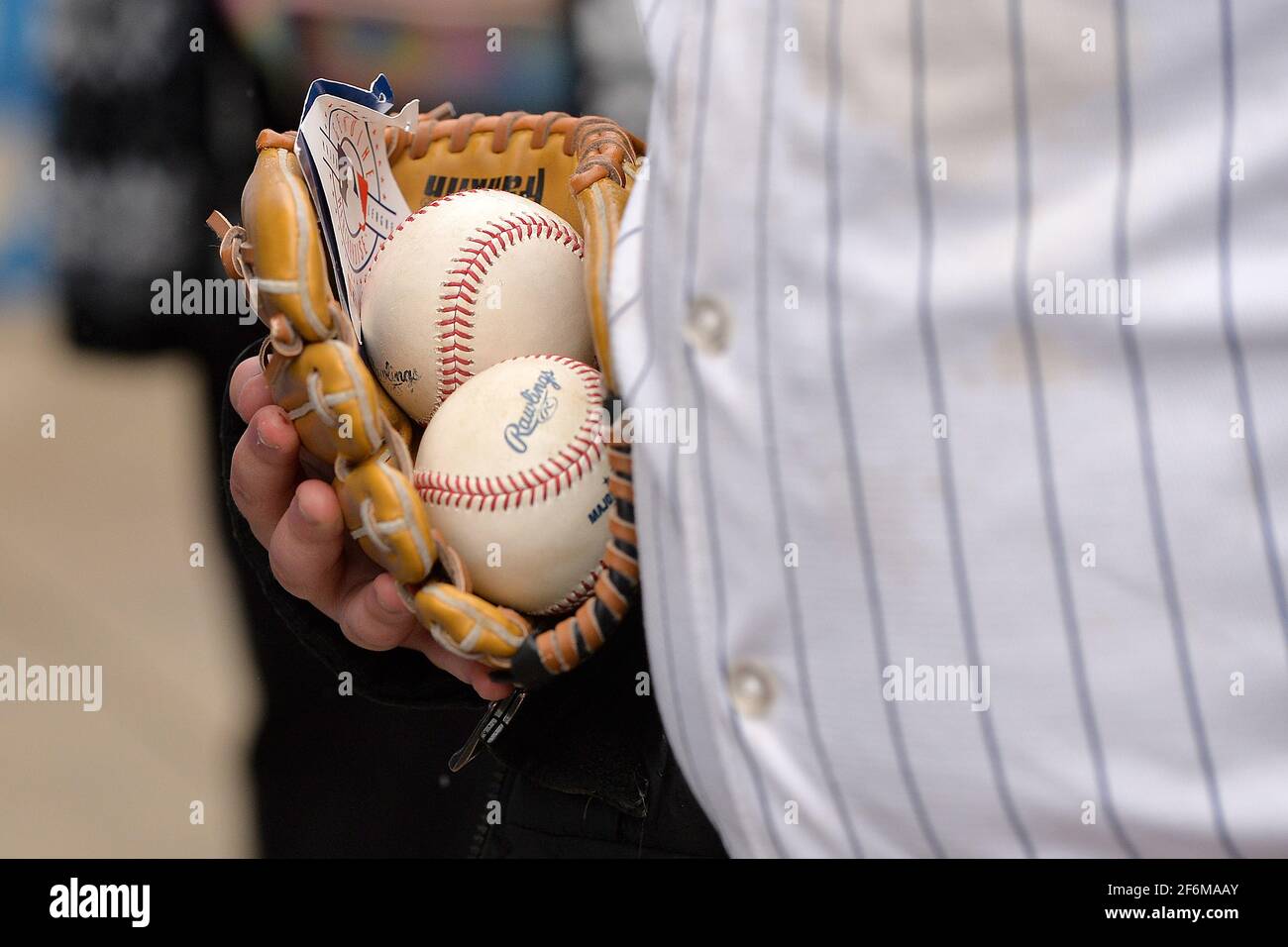 Un homme portant un maillot yankee à fines rayures et portant un gant de baseball et deux balles de baseball se tient en ligne pour assister au match de baseball des New York Yankees le jour d'ouverture contre les Blue Jays de Toronto dans le quartier Bronx de New York, NY, le 1er avril 2021. Fermeture complète la saison dernière en raison de la pandémie de COVID-19, un nombre limité de fans pourront assister au premier match à domicile, ayant besoin de fournir la preuve d'un test négatif de COVID-19, faire prendre leur température à l'entrée et porter un masque à l'intérieur du stade. (Photo par Anthony Behar/Sipa USA) Banque D'Images