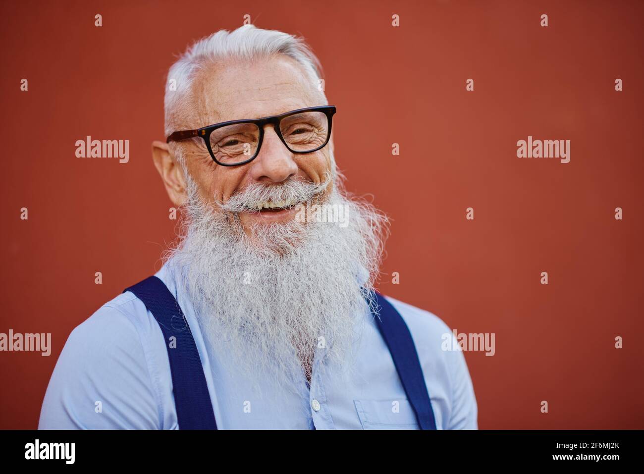 Homme hipster gai d'humeur accueillante posé sur le mur rouge Arrière-plan - personne à la mode dans des vêtements de mode décontractés - heureux concept de mode de vie des personnes âgées Banque D'Images