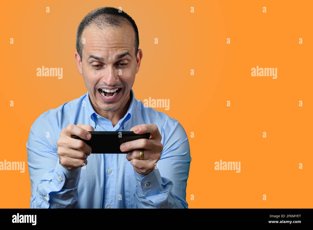 Homme mature en tenue formelle regardant son smartphone et célébrant avec le grand sourire. Arrière-plan orange. Banque D'Images