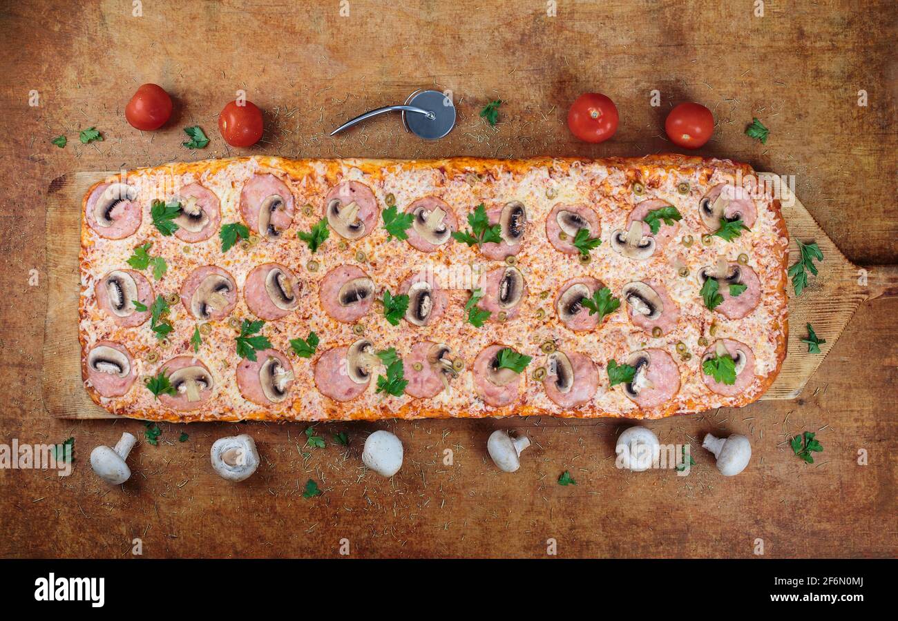 Une pizzeria d'un mètre une pizza longue avec du jambon et des champignons se trouve sur une table en bois. Pizza romaine sur une spatule en bois. Pizza d'un mètre de long. Banque D'Images
