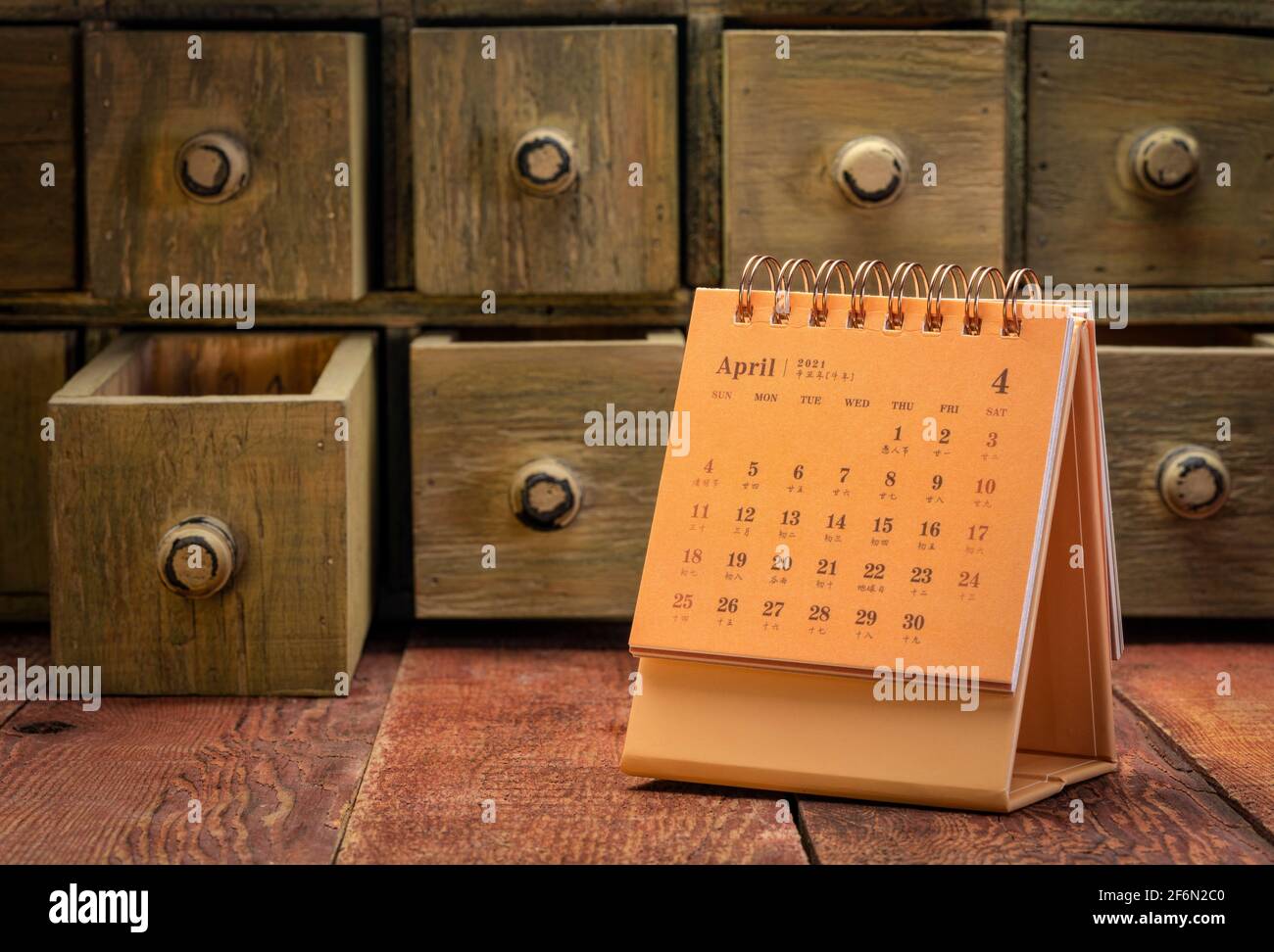 2021 avril - calendrier de bureau en spirale avec des symboles anglais et chinois sur une table en bois de grange avec des tiroirs d'apothicaire rustiques en arrière-plan, tim Banque D'Images