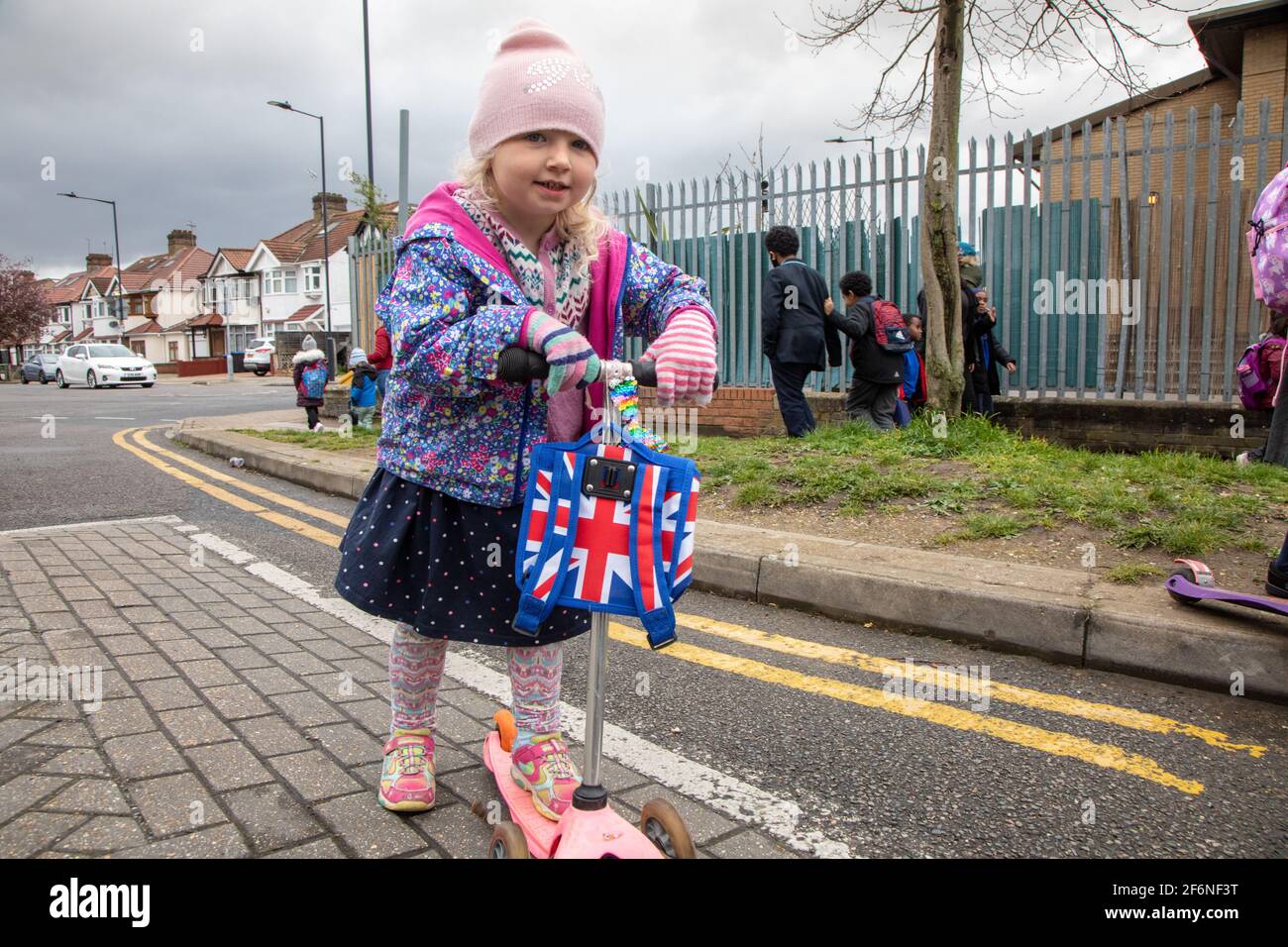 Une fille de trois ans sur un scooter avec un sac drapeau britannique, à l'extérieur d'une école à la maison Banque D'Images