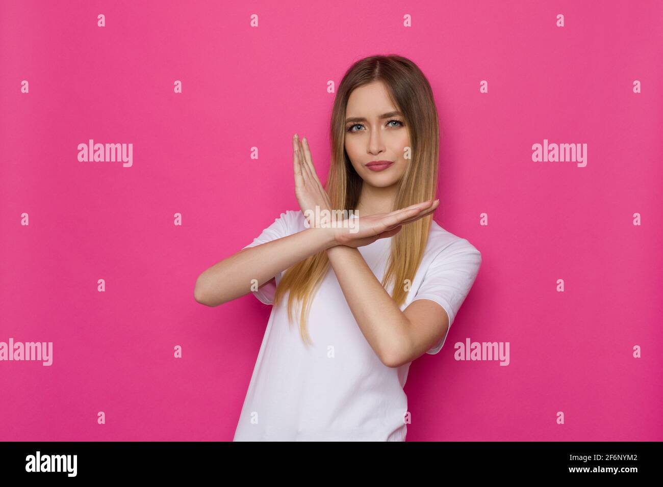 La jeune femme confiante ne montre AUCUN signe avec les mains croisées. Taille haute studio tourné sur fond rose. Banque D'Images