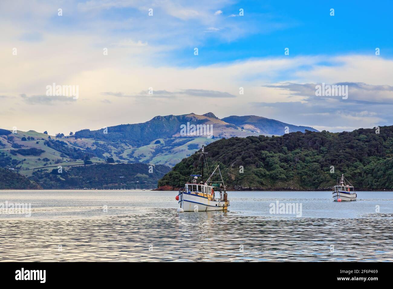 Bateaux de pêche dans le port d'Akaroa, en Nouvelle-Zélande, avec les montagnes de la péninsule de Banks en arrière-plan Banque D'Images