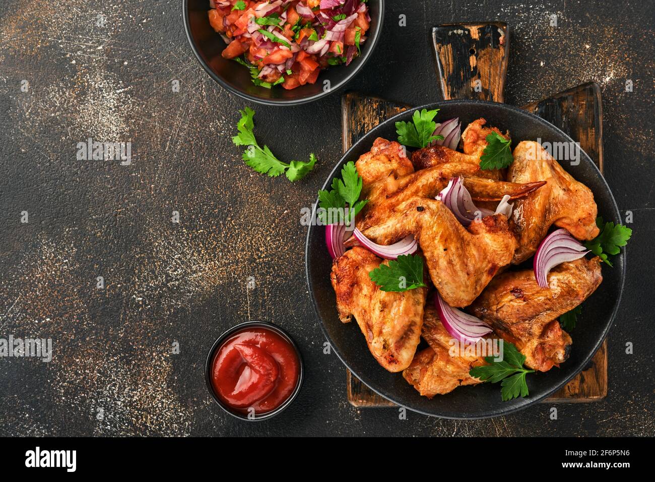 Ailes de poulet grillées ou barbecue grillé avec épices et sauce tomate salsa sur une assiette noire. Vue de dessus avec espace de copie. Banque D'Images