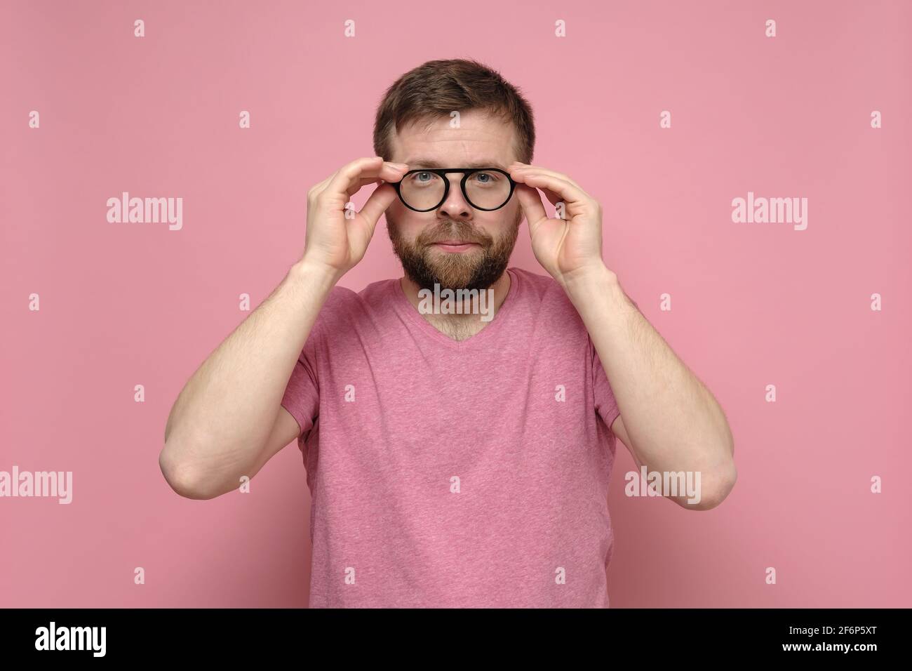 Homme caucasien avec une mauvaise vue essayant des lunettes, il choisit soigneusement les accessoires et les lentilles appropriés. Fond rose. Banque D'Images