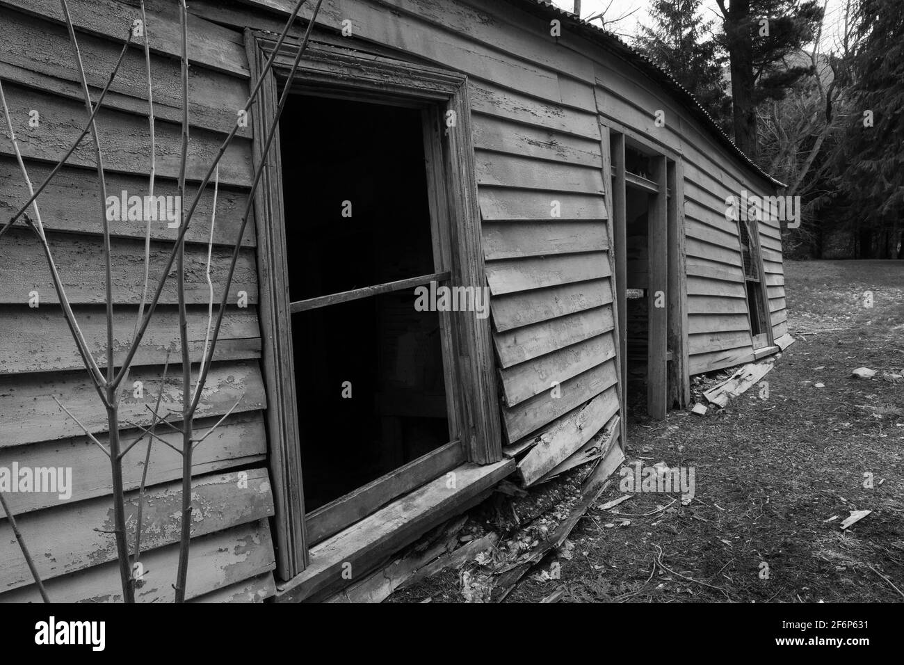 Les murs affaissés et les fenêtres vides d'une maison en bois abandonnée et abandonnée. Noir et blanc Banque D'Images