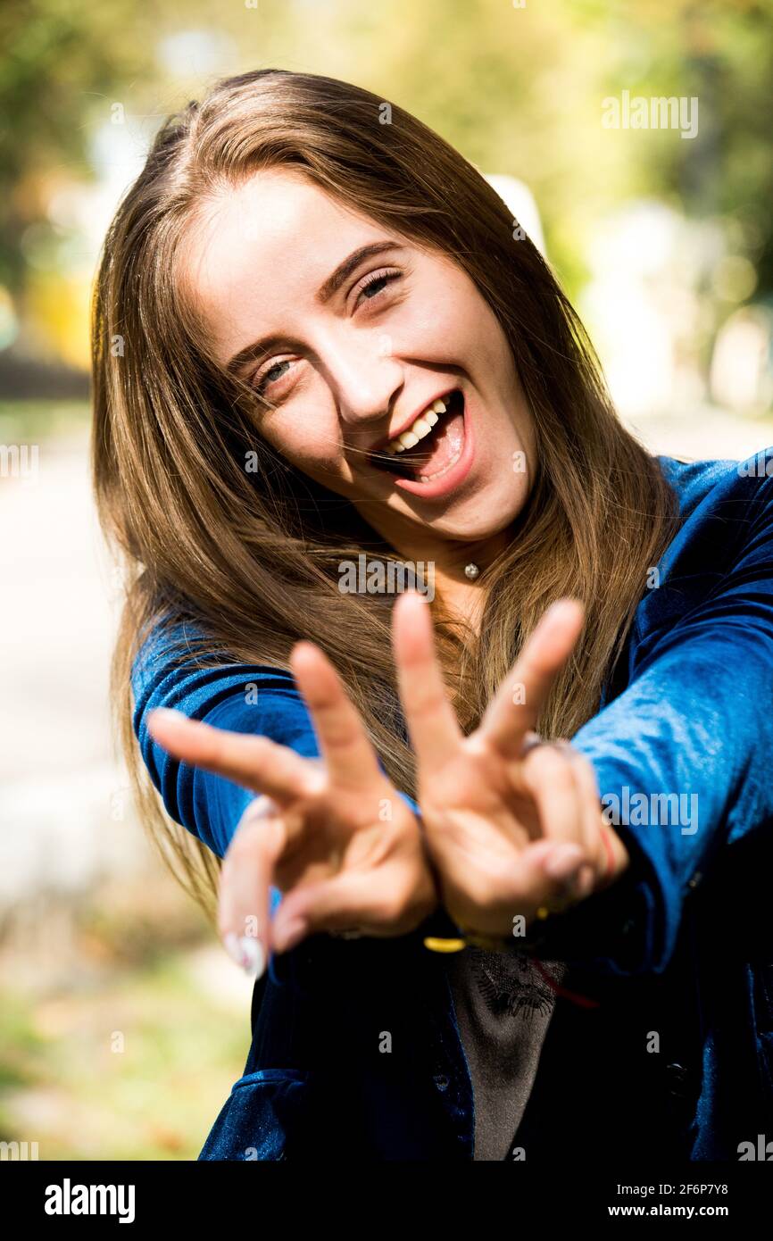 Jeune assez sexy courageuse russe/ukrainienne femme sourit dans l'appareil photo avec un regard joyeux sur son visage et les doigts sur les deux Mains disant V pour la victoire Banque D'Images