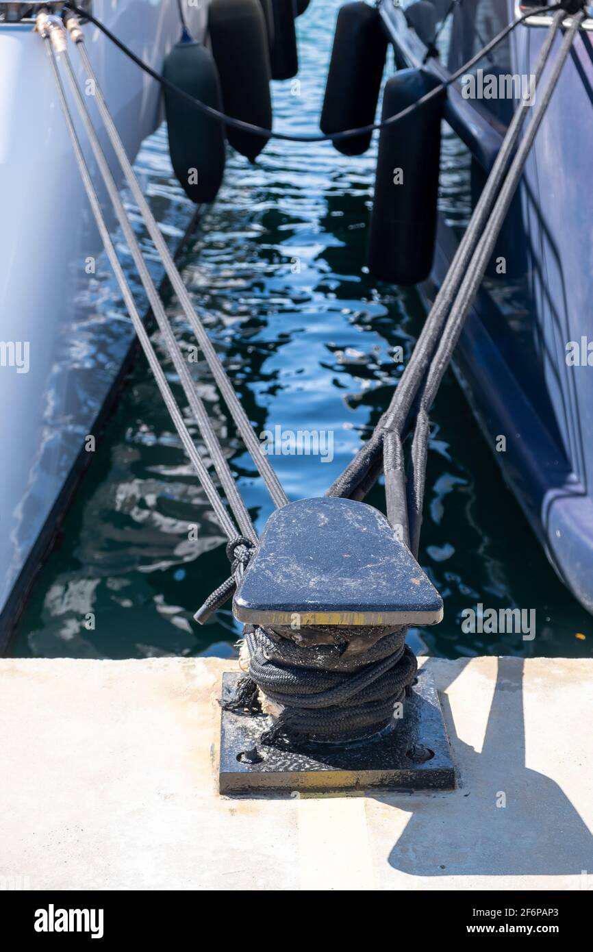 Cordes d'amarrage attachées sur un bollard en acier noir. Yachts amarrés sécurisés au quai du port à la marina de Flisvou, Grèce. Concept de bollard d'amarrage. Vertical, cl Banque D'Images