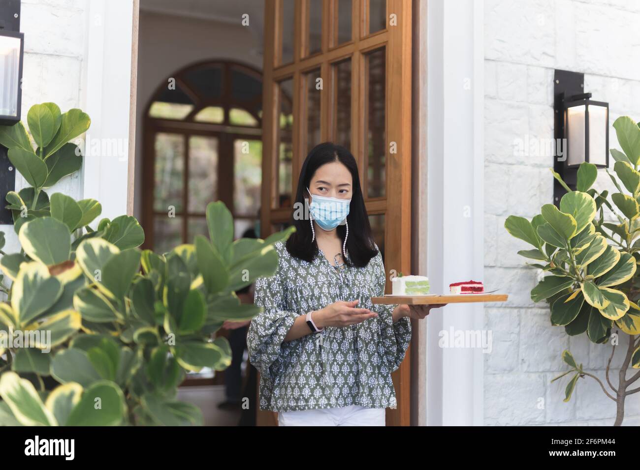 Femme dans le masque de protection servant une tranche de gâteau sur un plateau au client. Banque D'Images