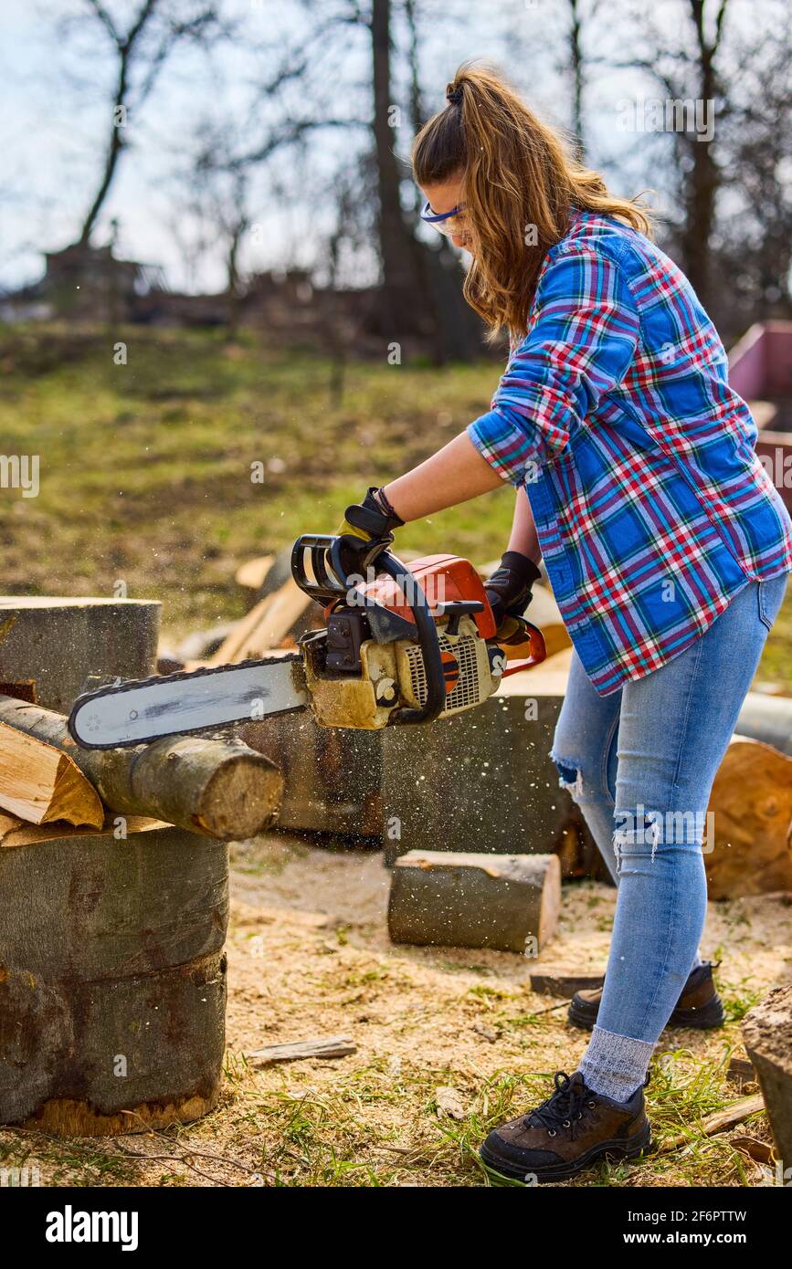 Jeune femme utilisant une tronçonneuse pour couper une bûche pour le bois  de chauffage Photo Stock - Alamy