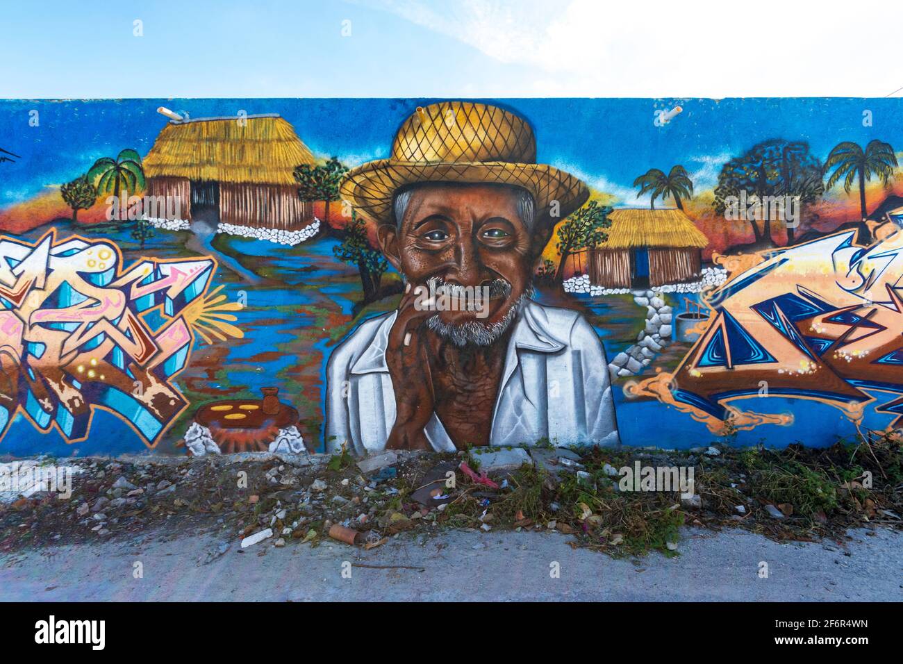 Art de rue dans une petite ville sur un long mur avec un vieil homme portant un chapeau de paille, une hutte rustique et des mots, avec un ciel bleu au-dessus du mur Banque D'Images