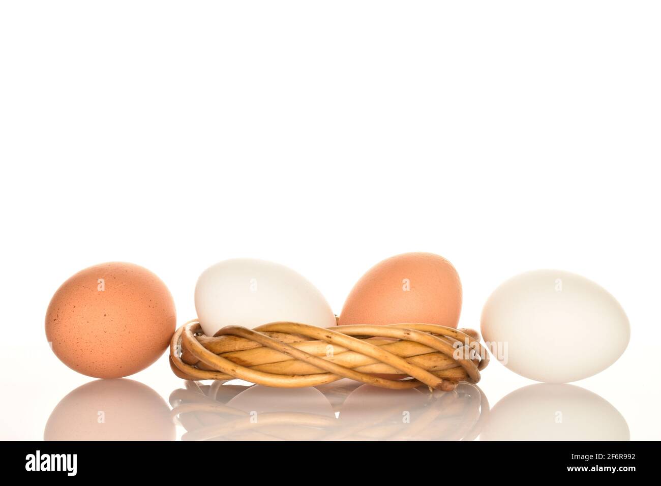 Quatre œufs de poulet frais bio délicieux, blancs et beiges, avec une couronne de brindilles sur fond blanc. Banque D'Images