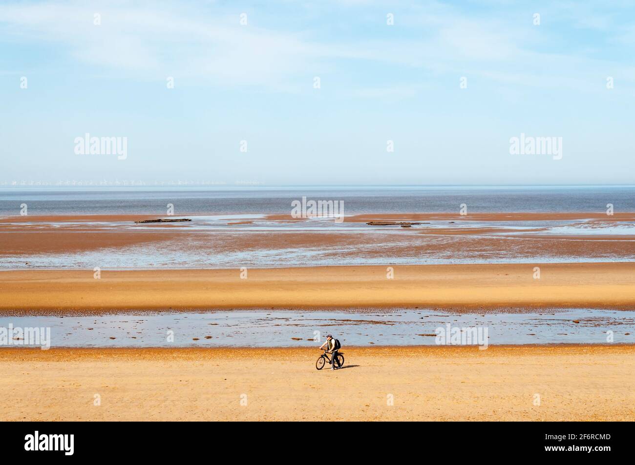 Un homme qui pousse un vélo le long d'une plage vide et déserte à Holme-Next-the-Sea sur la côte nord de Norfolk. Banque D'Images
