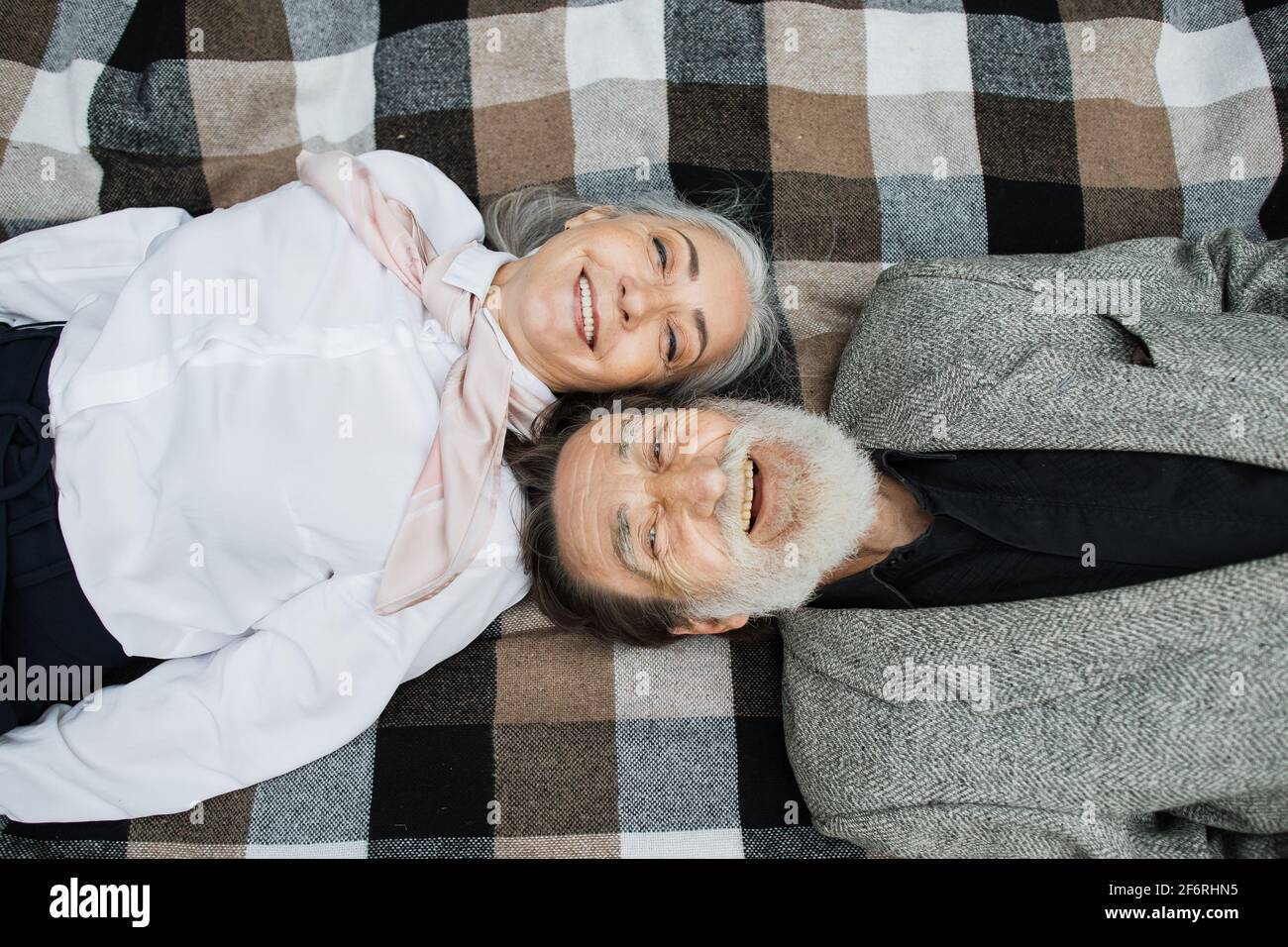 Vue de dessus d'un couple d'âge mûr caucasien allongé tête à tête sur une couverture à damier et souriant sur l'appareil photo. Bonne retraite. Amour pour les âges. Banque D'Images