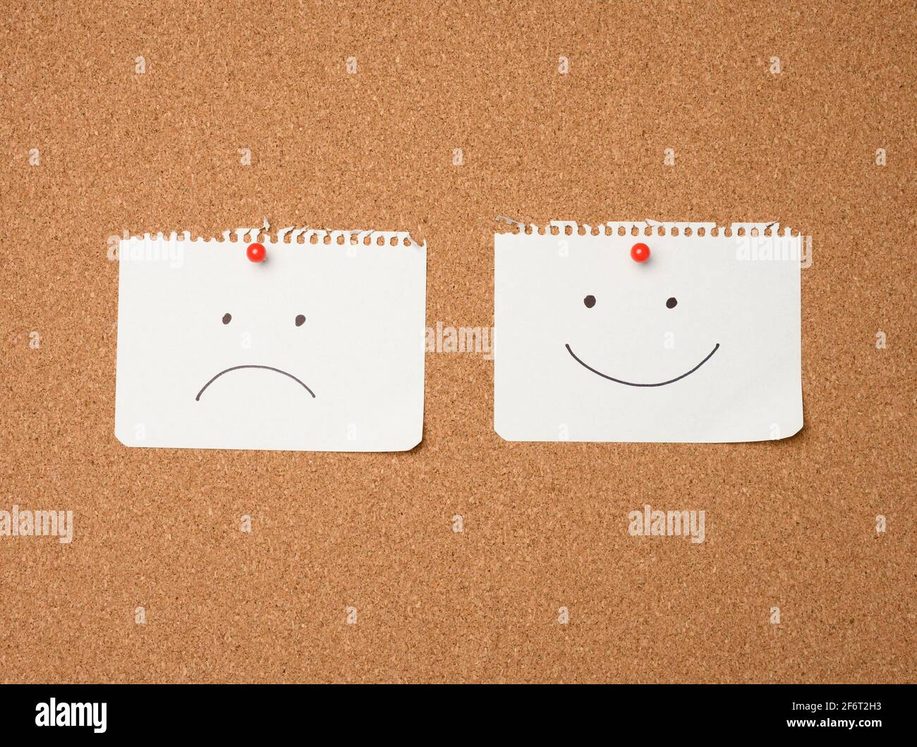 deux feuilles de papier avec un sourire et une triste émotion attachée avec un bouton sur un tableau marron, la joie et la dépression. Banque D'Images