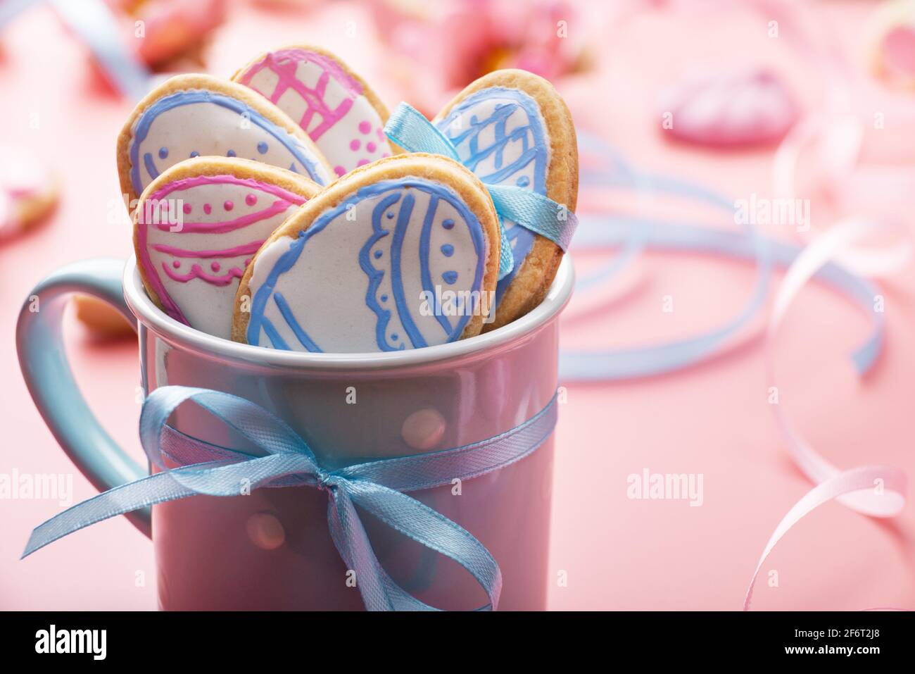 Fond de cuisson de Pâques de biscuits givrés en forme d'oeuf dans une tasse bleue sur fond rose. Banque D'Images