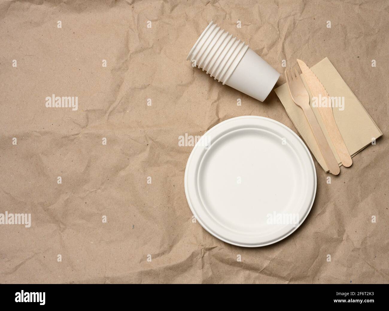 assiettes et tasses en papier blanc rondes jetables sur fond de papier marron, vue de dessus, zéro déchet. Banque D'Images