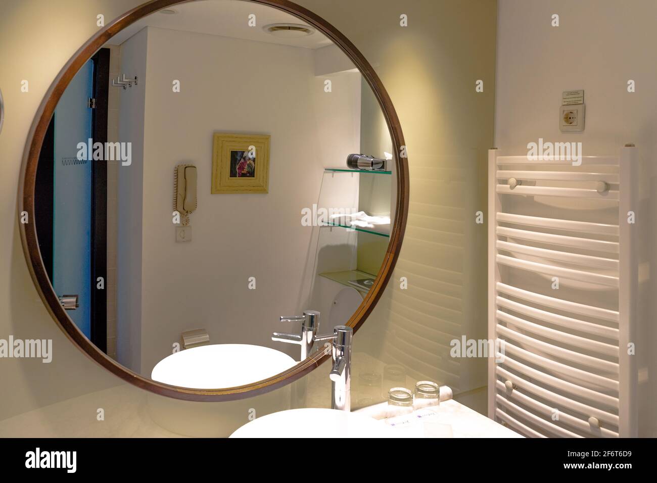 Un grand miroir rond dans l'intérieur moderne de la salle de bains dans un appartement ou un hôtel, avec le lavabo et le robinet réfléchi Banque D'Images