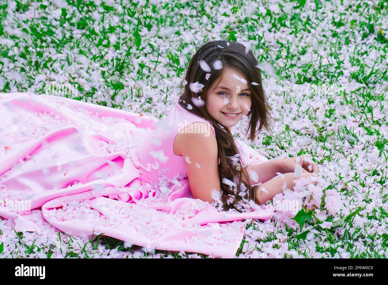 Belle petite fille en robe rose avec visage souriant couché sur l'herbe  verte couverte de pétales de fleur de printemps à l'extérieur Photo Stock -  Alamy