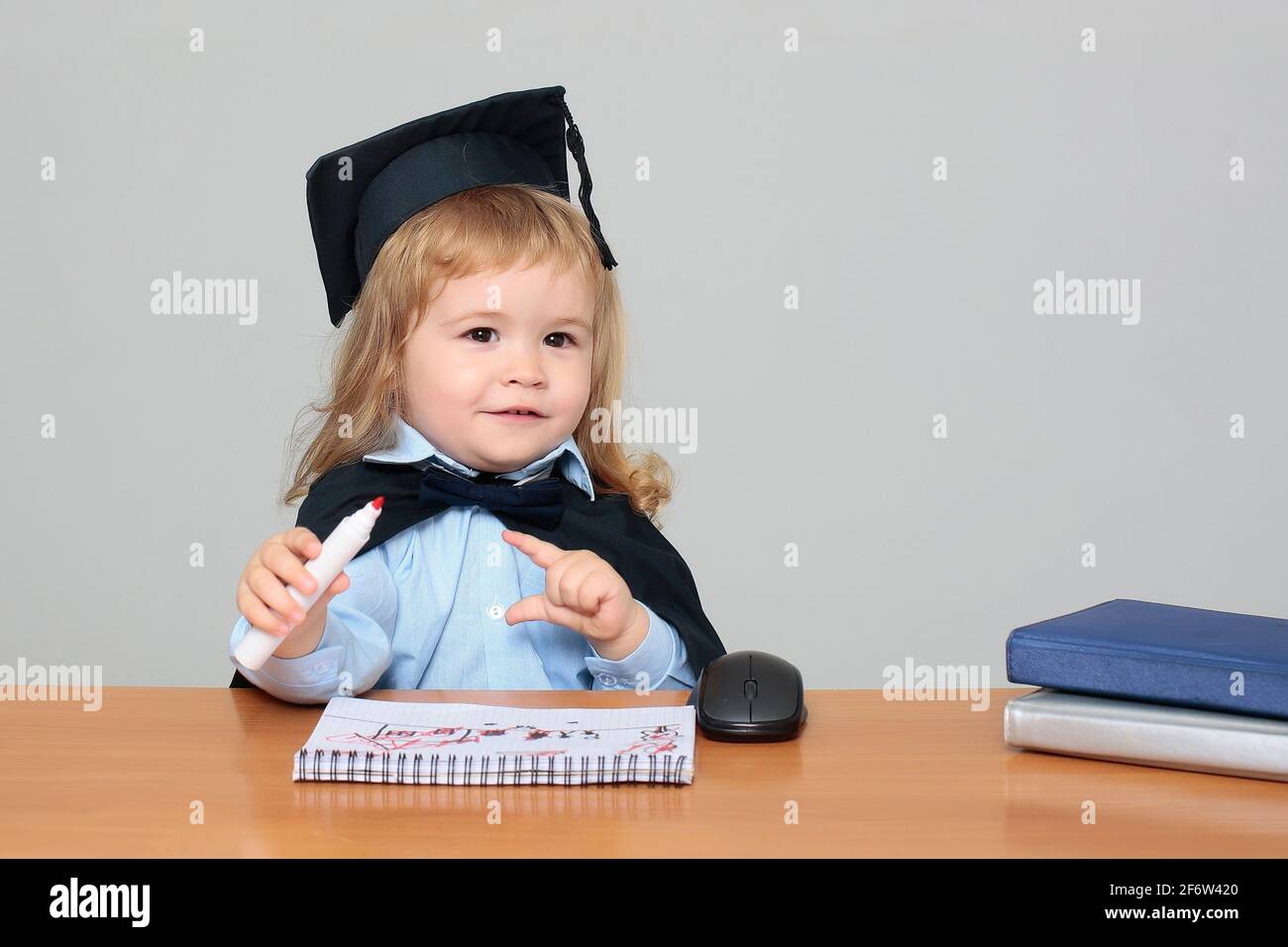 Enfant bébé dans le manteau académique et la casquette assis à l'école  bureau en bois tenant la marque Photo Stock - Alamy