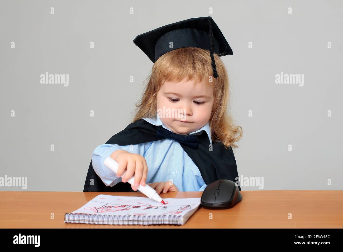 Petit Enfant Etudiant En Robe De Graduation Et Chapeau Au Bureau D Ecole Dessin Dans Le Livre De Note Par Marqueur Photo Stock Alamy