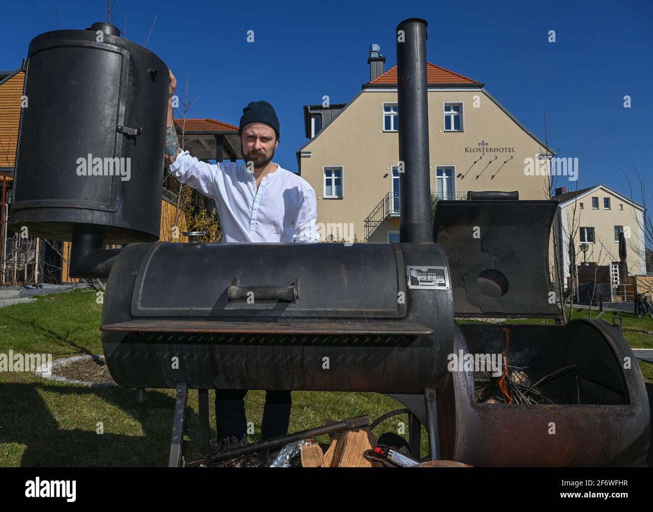 30 mars 2021, Brandebourg, Neuzelle: Manu Bunke, chef de cuisine au Wilde Klosterküche se dresse derrière un fumeur dans le jardin en face de l'hôtel. De nombreux restaurants restent au-dessus de l'eau dans la crise de Corona avec des plats à ramasser ou à livrer. Le Wilde Klosterküche de Neuzelle, dans le quartier Oder-Spree, propose des événements et des menus à Pâques, par exemple, mais pas de menu de déjeuner régulier. « pour nous, le niveau de prix est trop bas pour qu'il soit valable », a déclaré le chef Manu Bunke, qui affirme qu'il accorde un excellent rapport qualité/prix aux produits régionaux. « que nous puissions exister sur ce n'est pas le cas. » H Banque D'Images