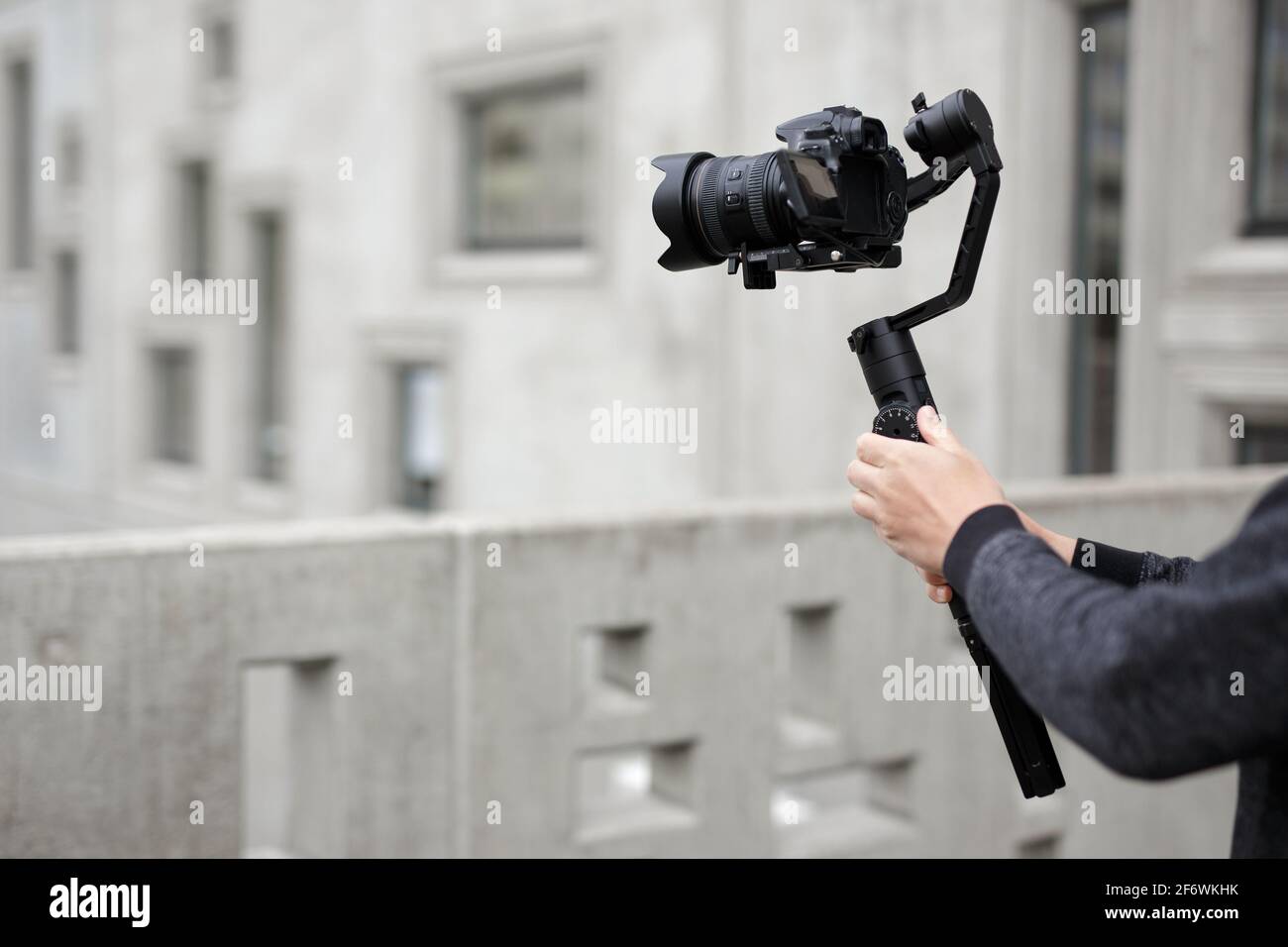 concept de réalisation, de loisirs et de créativité - appareil photo reflex numérique moderne sur nacelle 3 axes dans les mains des hommes sur fond de bâtiment en béton Banque D'Images