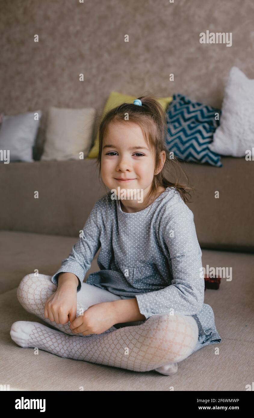 une petite fille dans une robe grise est assise sur le canapé et sourit.  environnement à la maison Photo Stock - Alamy
