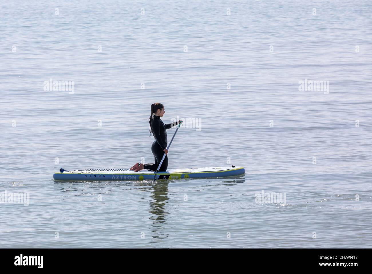Une dame solitaire paddle-boarder s'agenouillant sur sa planche Banque D'Images