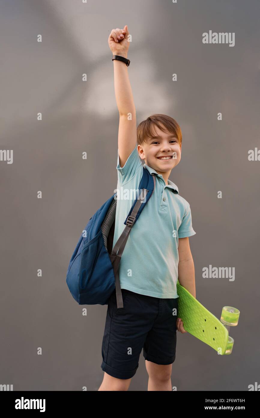 Jeune GARÇON D'ÉCOLE avec sac à dos posant avec PENNY BOARD, la main vers  le haut sur fond gris Photo Stock - Alamy