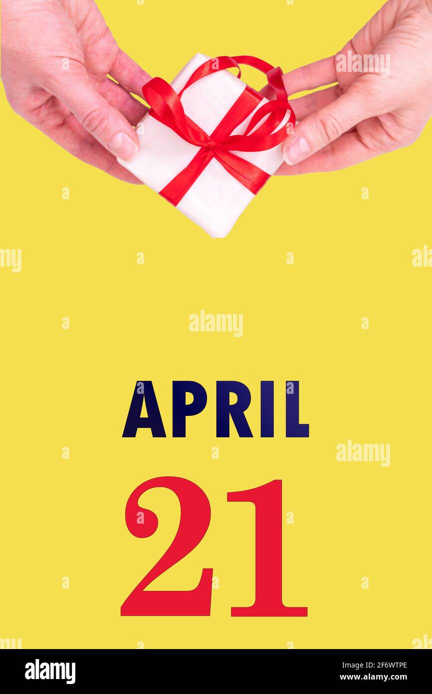 21 avril. Calendrier vertical de fête avec mains tenant boîte cadeau blanche avec ruban rouge et calendrier Date 21 avril sur fond jaune lumineux. Banque D'Images