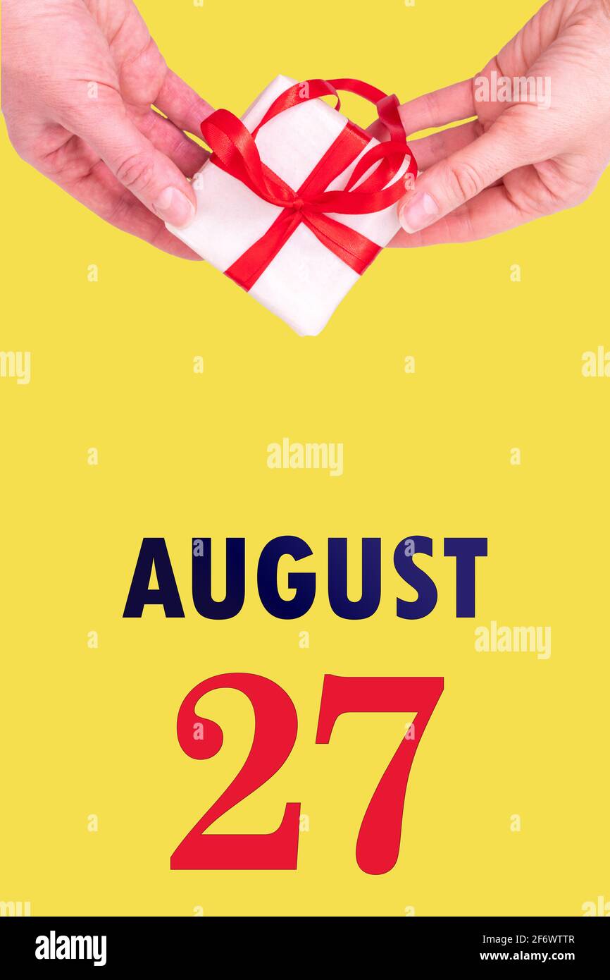 27 août. Calendrier vertical de fête avec mains tenant boîte cadeau blanche avec ruban rouge et calendrier Date 27 août sur fond jaune lumineux Banque D'Images