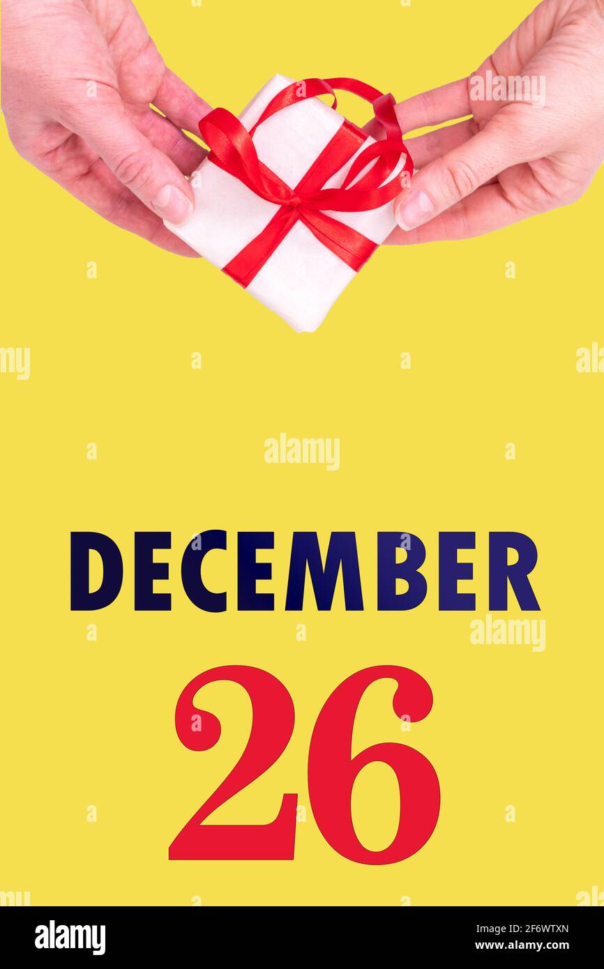26 décembre. Calendrier vertical de fête avec mains tenant boîte cadeau blanche avec ruban rouge et calendrier Date 26 décembre sur fond jaune illuminant Photo Stock - Alamy