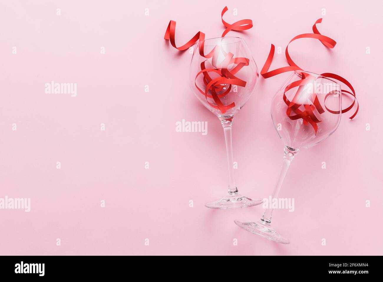 Deux verres à vin et un ruban rouge sur un rose Arrière-plan avec espace de copie - engagement ou fête d'anniversaire Concept - carte lumineuse pour un lieu Banque D'Images