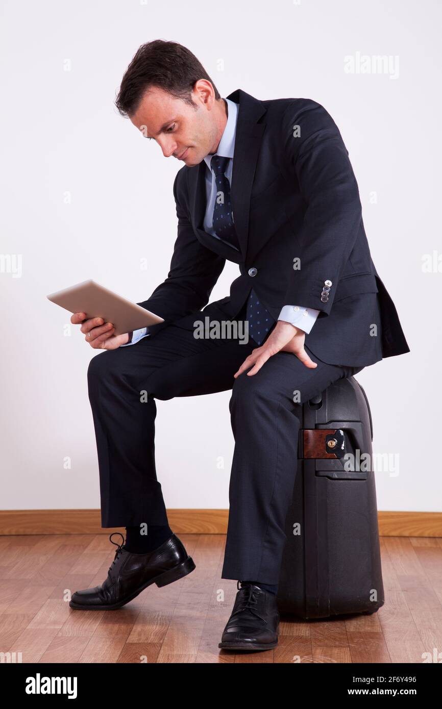 Un homme d'affaires s'assoit sur un bagage de voyage à l'aide d'une tablette numérique Banque D'Images