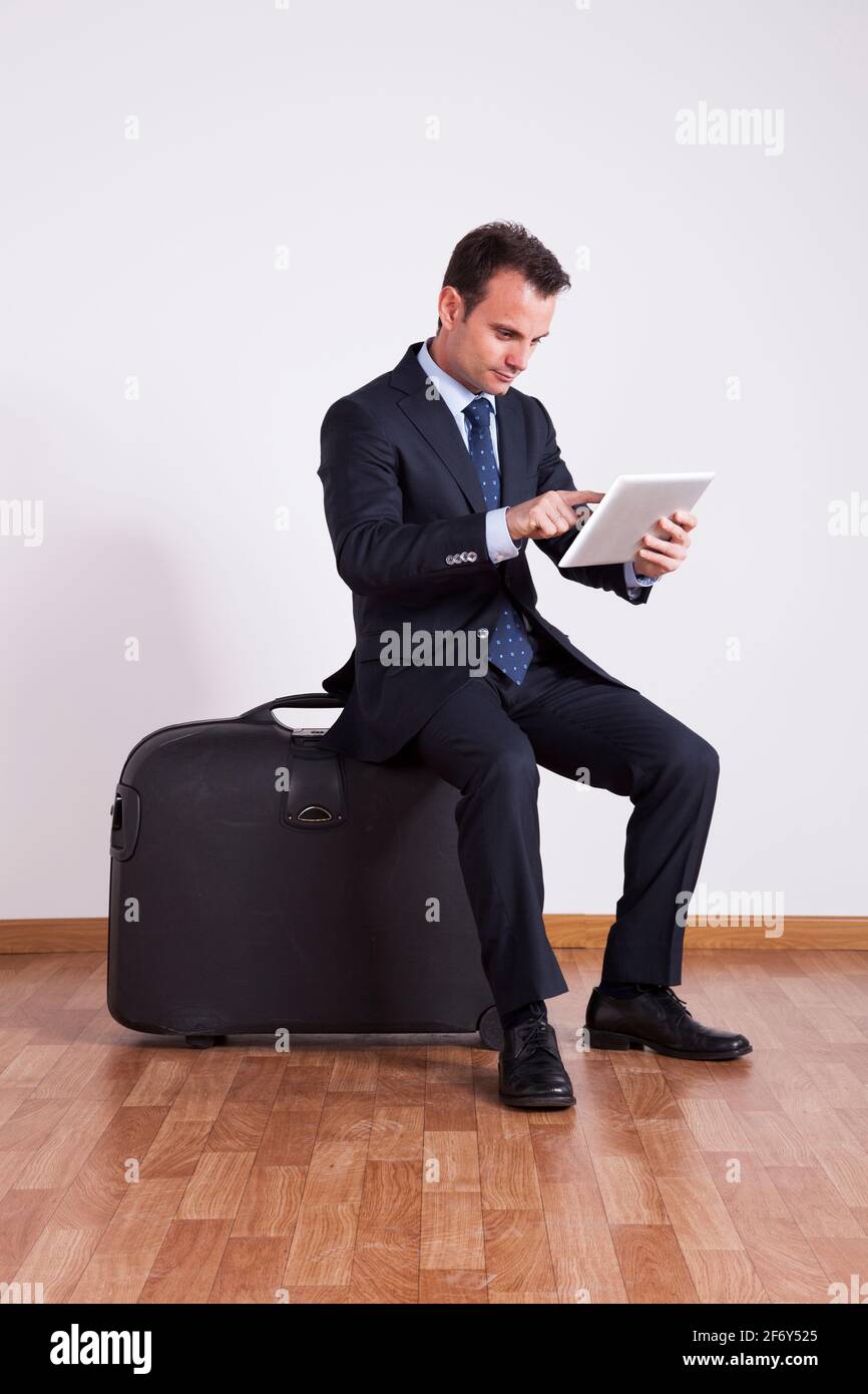 Un homme d'affaires s'assoit sur un bagage de voyage à l'aide d'une tablette numérique Banque D'Images