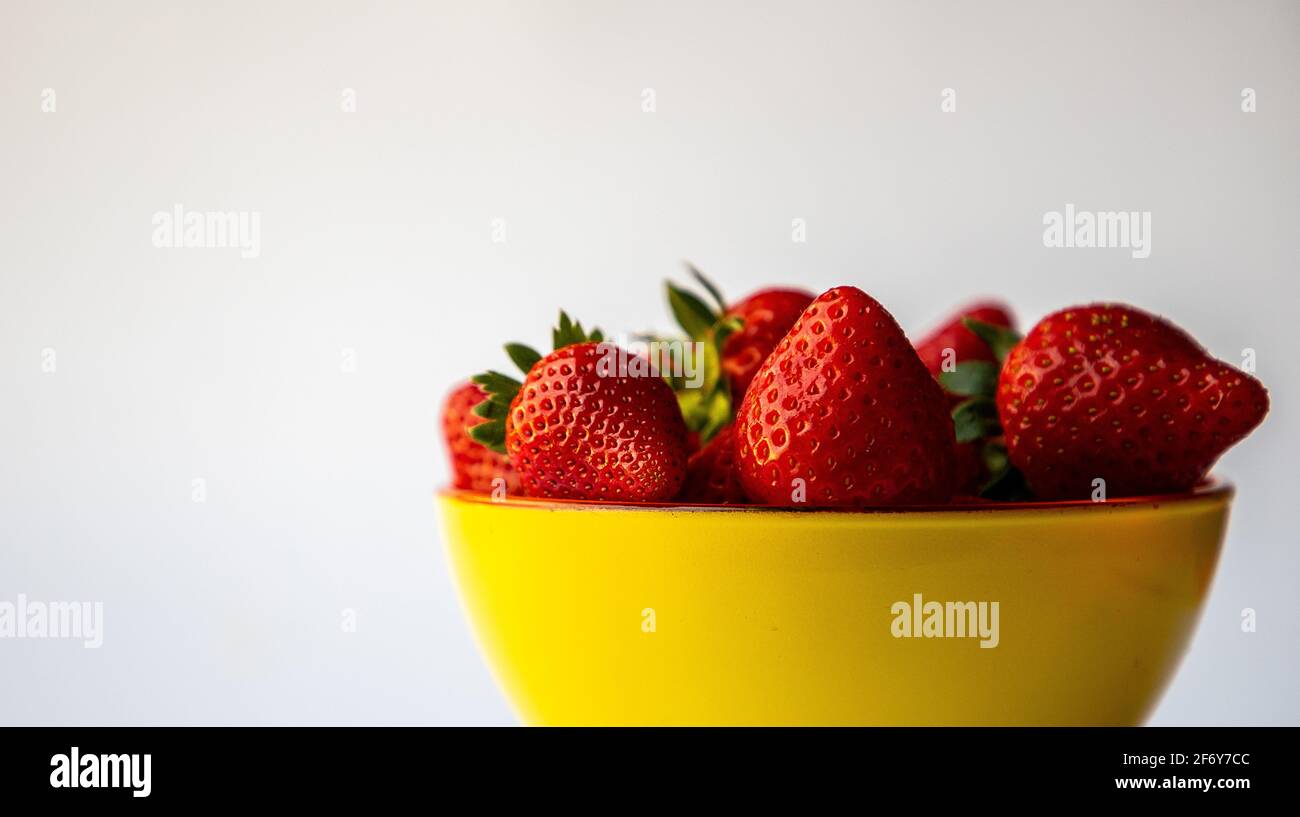 Fraises rouges dans un bol jaune, fond blanc Banque D'Images