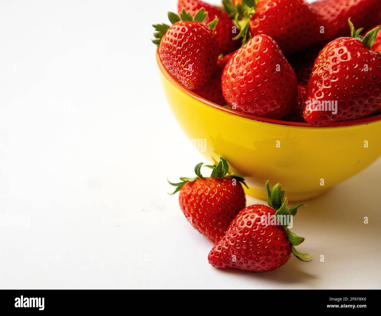 Fraises rouges dans un bol jaune, fond blanc Banque D'Images