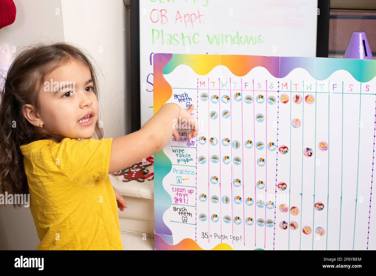 Tableau de motivation des tâches pour une fille de quatre ans, elle pointe sur le tableau et parle de tâche Banque D'Images
