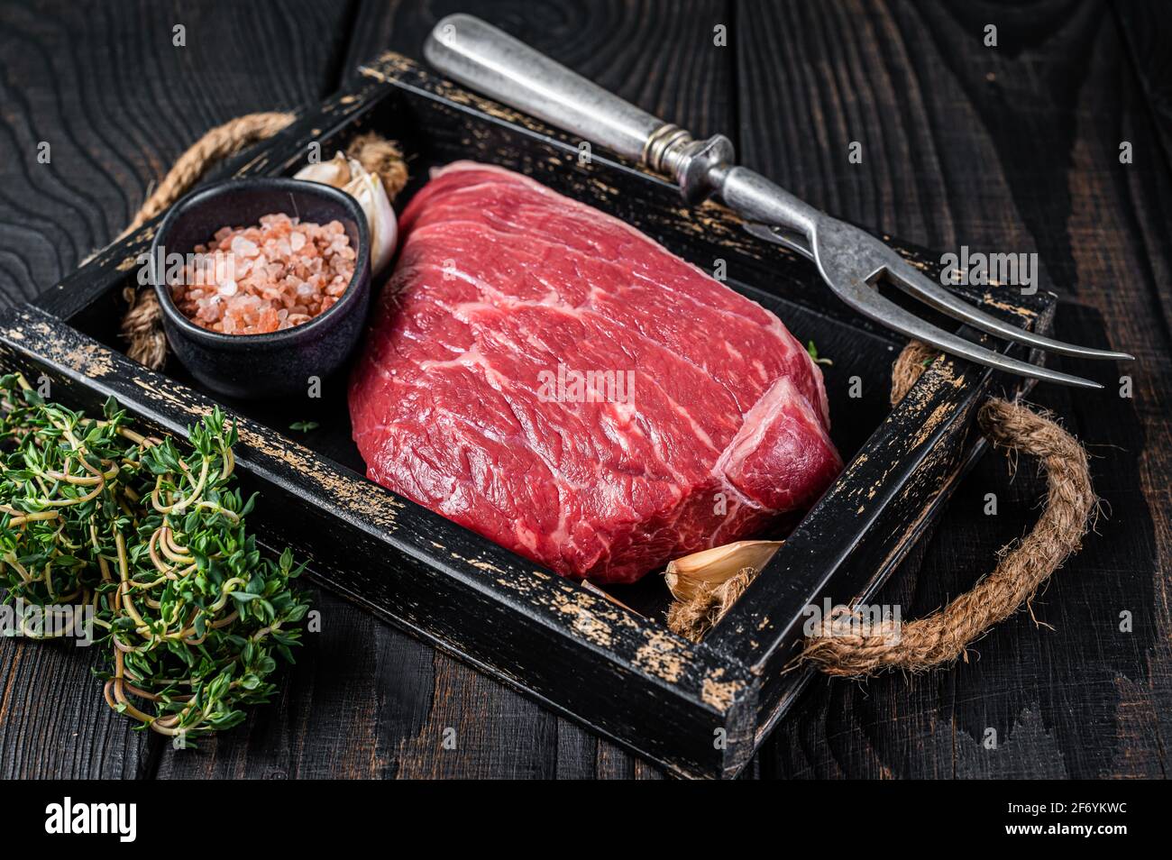 Steak de viande de bœuf coupé au sommet de la sirloine crue ou Picanha dans un plateau en bois avec des herbes. Arrière-plan en bois noir. Vue de dessus Banque D'Images