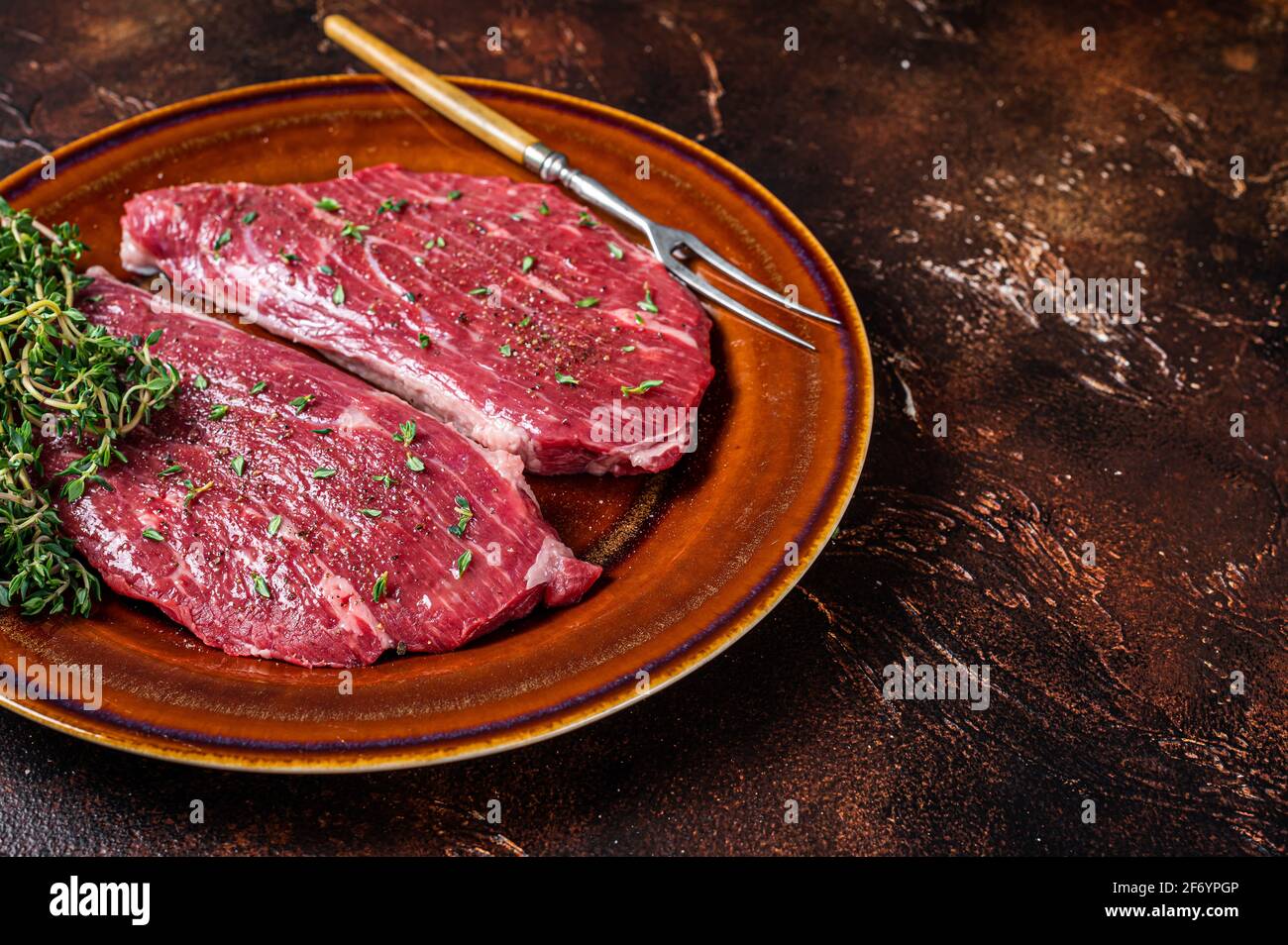 Steak de calotte cru ou steak d'aloyau dans une assiette rustique au thym et à l'huile d'olive. Arrière-plan sombre. Vue de dessus. Copier l'espace Banque D'Images