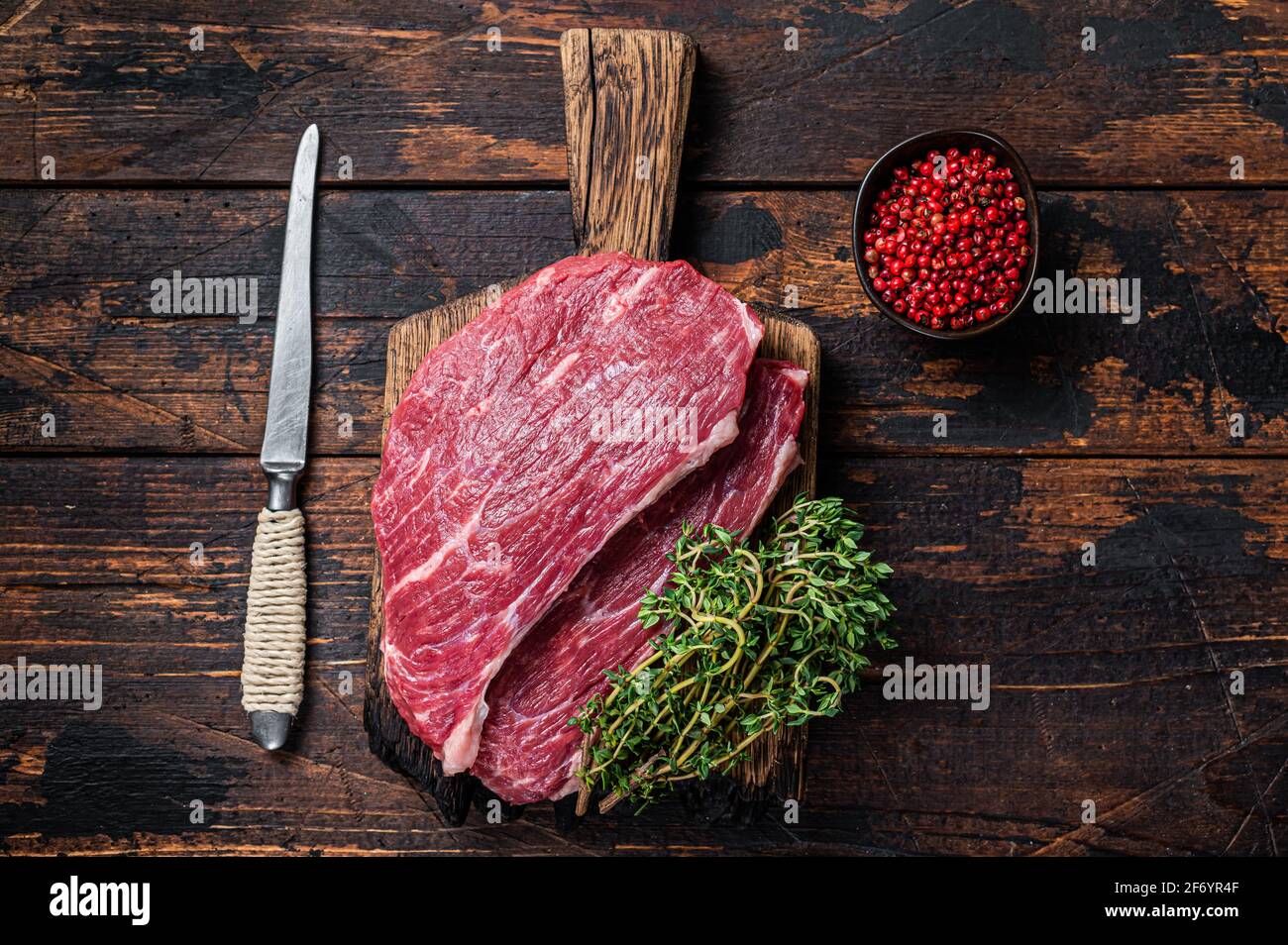 Steak de chapeau de sirloin cru ou steak de Picanha sur une planche de bois au thym. Arrière-plan en bois sombre. Vue de dessus Banque D'Images