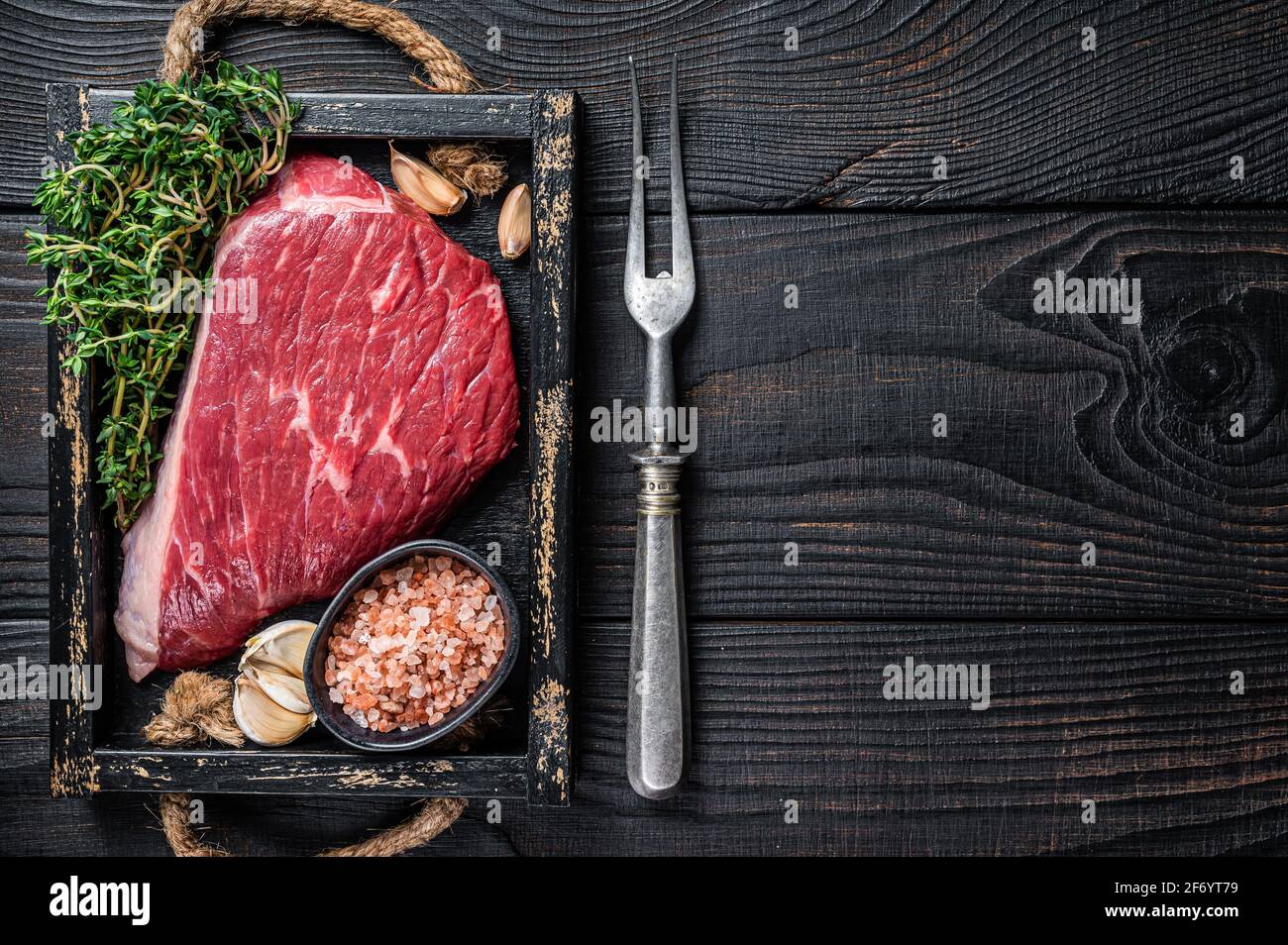 Steak de viande de bœuf coupé au sommet de la sirloine crue ou Picanha dans un plateau en bois avec des herbes. Arrière-plan en bois noir. Vue de dessus. Copier l'espace Banque D'Images