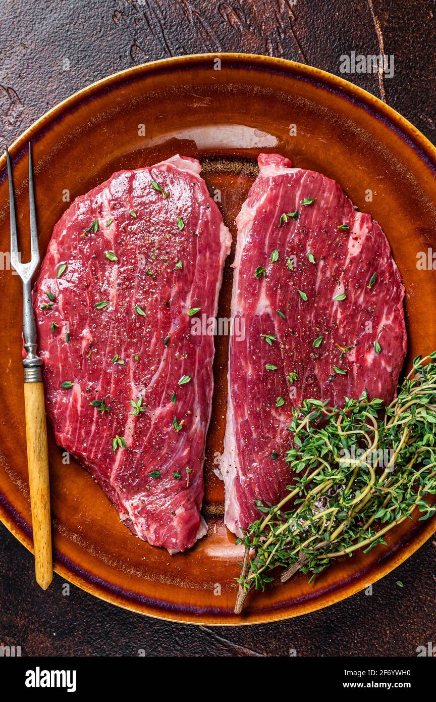 Steak de calotte cru ou steak d'aloyau dans une assiette rustique au thym et à l'huile d'olive. Arrière-plan sombre. Vue de dessus Banque D'Images